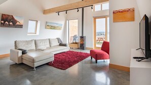A modern living room with a sofa, a red chair, a fireplace, and artwork on the walls. - Avonside Alpine Estate - Jindabyne (Avonside)