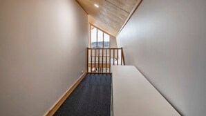 A narrow stairway with a wooden railing, carpeted steps, and a view of a landscape through a large window at the top.