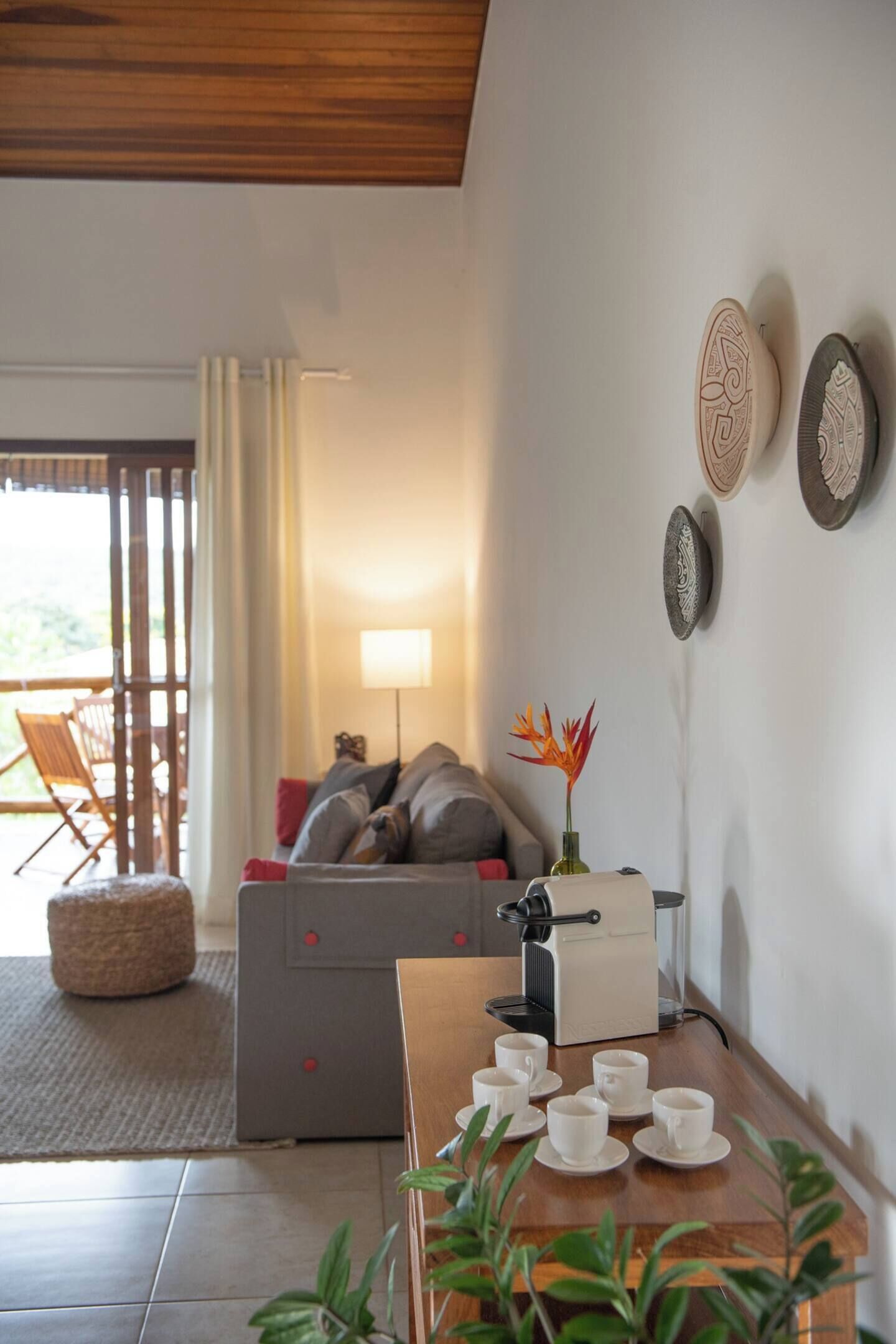 Een gezellige zithoek met een bank, een bijzettafeltje met kopjes, een lamp en decoratieve borden aan de muur.