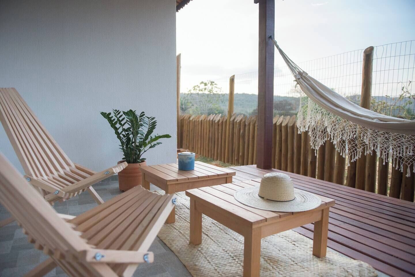 A wooden deck with two lounge chairs, a small table, a potted plant, and a hammock.