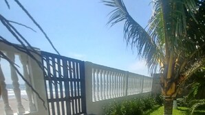 Un camino pavimentado que conduce a una entrada portonada, con una palmera y un muro blanco decorado con paneles.