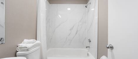 Un baño con inodoro blanco, lavamanos y bañera con cortina de ducha.