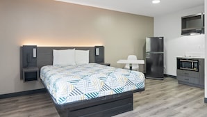 Ett modernt hotellrum med en säng, sängbord, ett litet skrivbord, ett kylskåp och en mikrovågsugn.