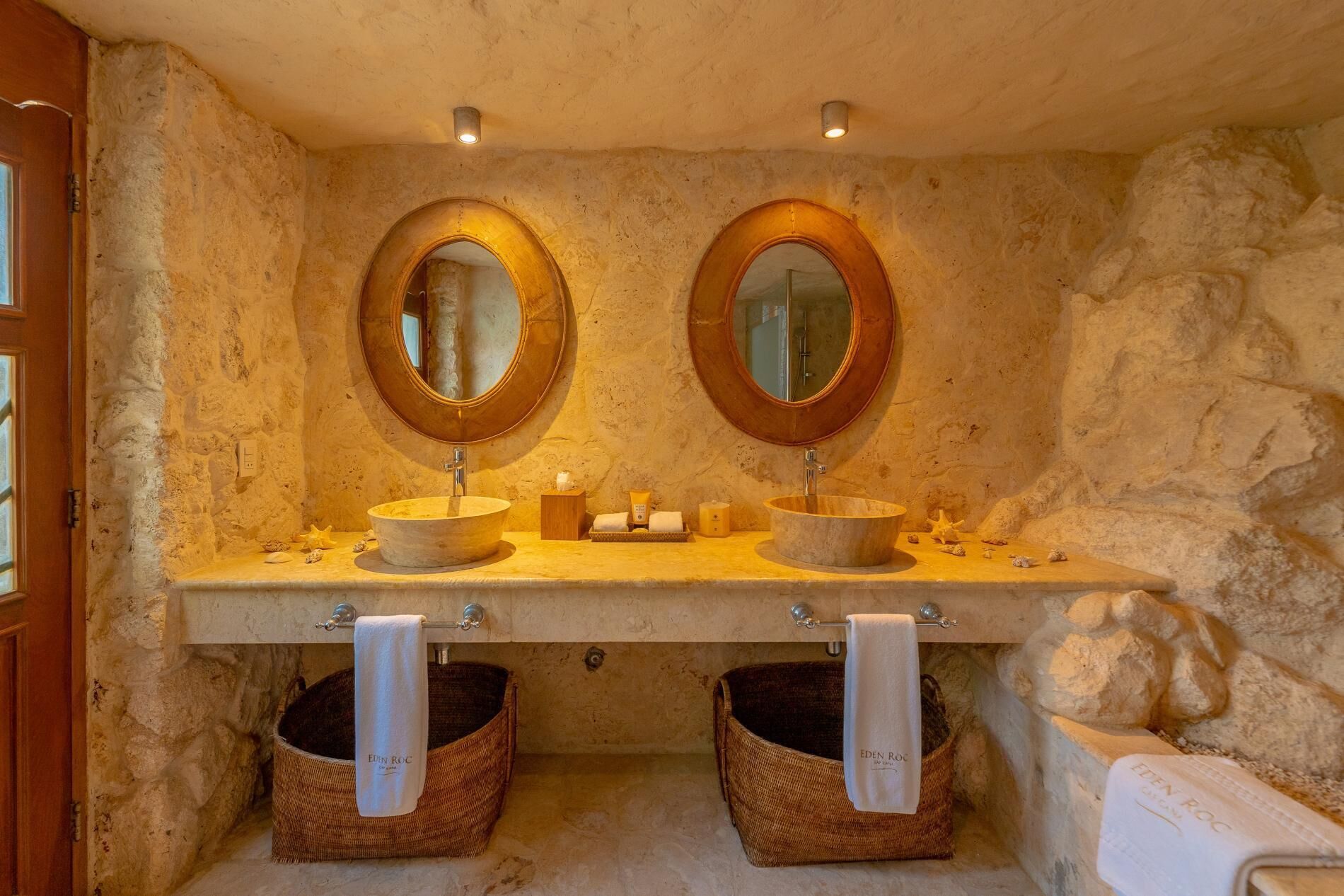 A bathroom with two sinks, each with a round mirror and a wooden countertop. There are two baskets under the sinks and a towel hanging on the wall.