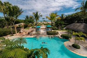 Ein Hotelpool mit klarem Wasser, umgeben von Palmen und einer Struktur mit Reetdach.