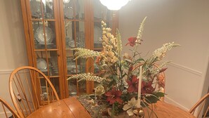 Una mesa de comedor de madera con sillas, un centro de mesa floral y un aparador de vidrio al fondo.