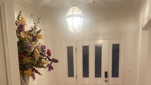 Un pasillo con piso de madera, paredes blancas, un arreglo floral decorativo y una puerta doble con paneles de vidrio esmerilado.