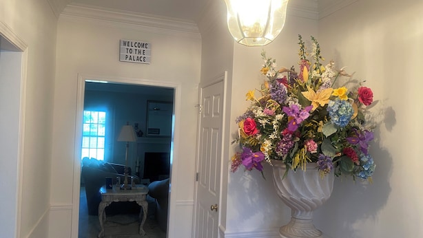 Un pasillo con un cartel que dice 'Welcome to the Palace', un gran arreglo floral y una araña.