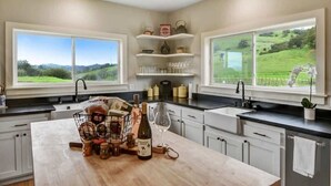 A modern kitchen with a large island, built-in shelves, and large windows offering a view of a green landscape. - Cottage Retreat at Paradise Ridge by Kohmsa (Santa Rosa)