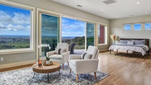 A spacious room with large windows, a bed, two armchairs, and a small round table. - Paradise Ridge Vineyard Retreat - Hot Tub & Views (Santa Rosa)