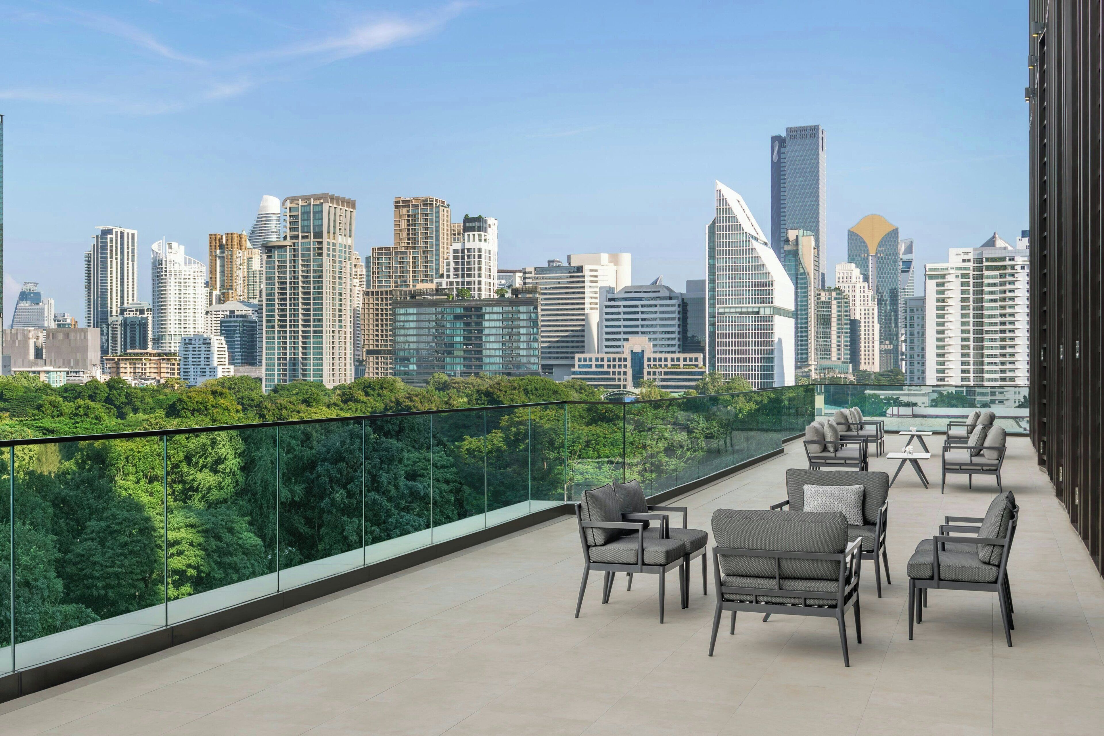 Een terras op het dak met buitenmeubilair, een glazen balustrade en uitzicht op de skyline van de stad.