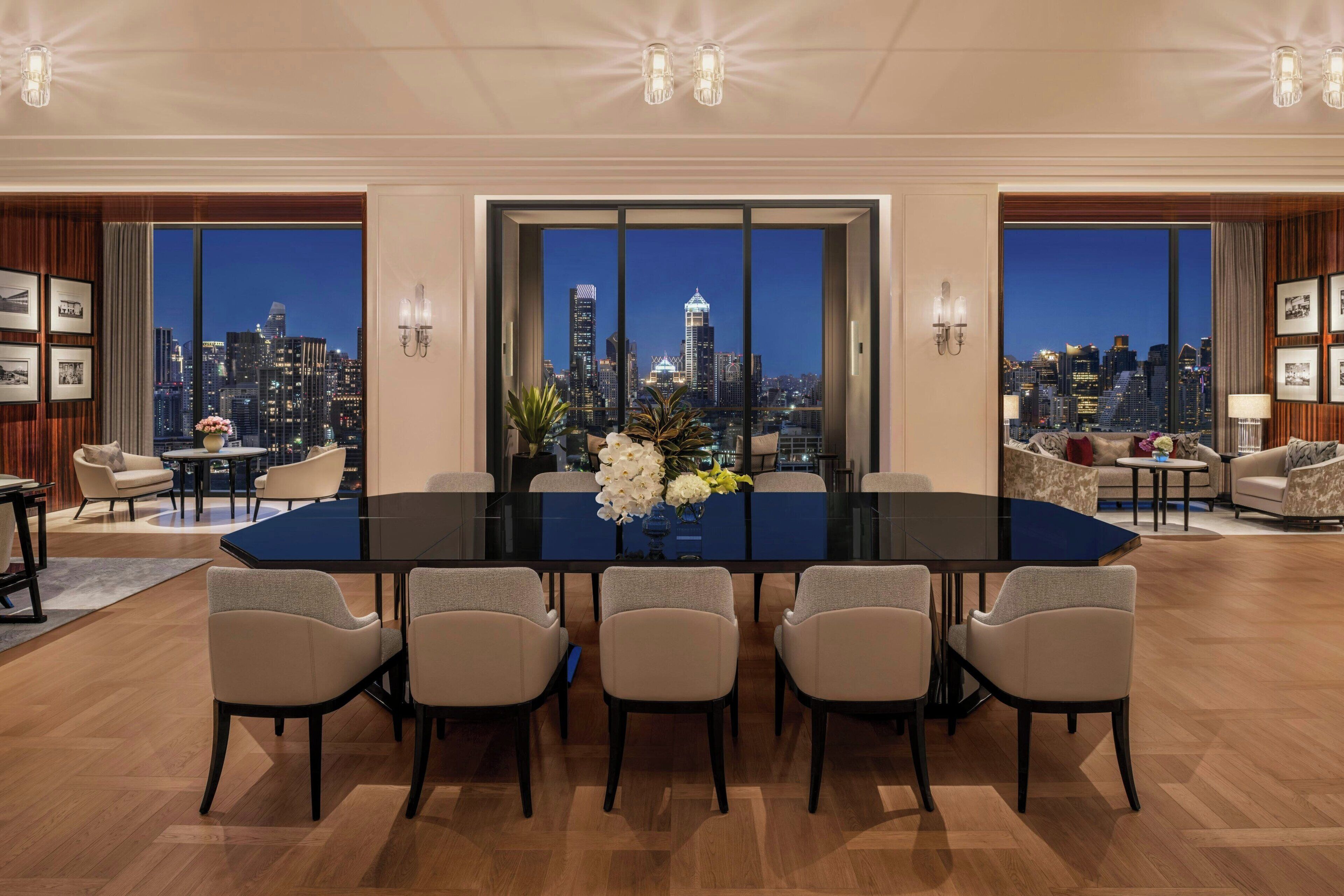 Un vaste espace de salle à manger avec une grande table et des chaises, une vue sur la ville grâce à de grandes fenêtres du sol au plafond, et un aménagement intérieur moderne.