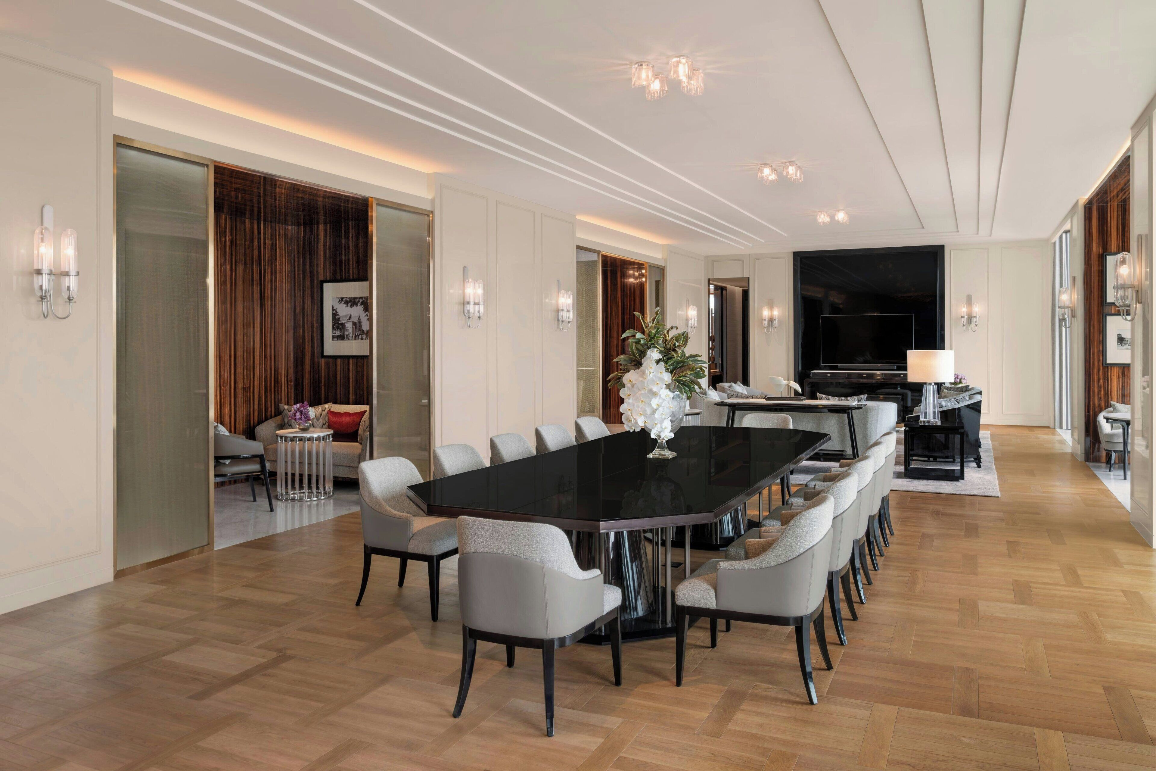 A spacious dining area with a long table and multiple chairs, a television, and a piano in the background.
