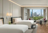 A hotel room with two beds, a small table, and a view of a cityscape.