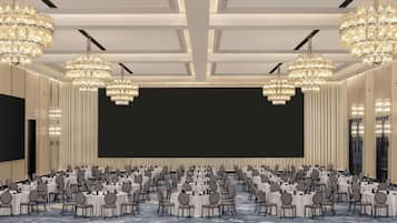 Un amplio salón de conferencias con filas de mesas y sillas redondas, una gran pantalla y múltiples candelabros.
