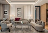 A modern living room with a sofa, armchairs, a coffee table, and a TV. There are framed pictures on the wall and a lamp on a side table.
