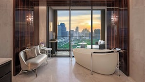 Een moderne badkamer met een groot bad, een bank en een uitzicht op een stadsbeeld bij zonsondergang.