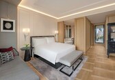 A modern hotel room with a large bed, bedside tables, a bench, a mirror, and a view of the city.
