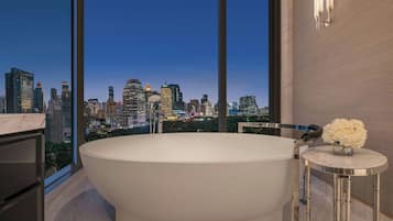 A modern bathroom with a freestanding bathtub, a marble vanity, and a view of a city skyline at dusk.