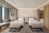 A hotel room with two beds, a sofa, a nightstand with lamps, and a large mirror.