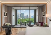 A hotel room with a large window, a bed, a round table, two chairs, and a small table with a vase of flowers.