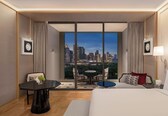 A hotel room with a large bed, a small dining table, two chairs, a sofa, and a view of a cityscape.