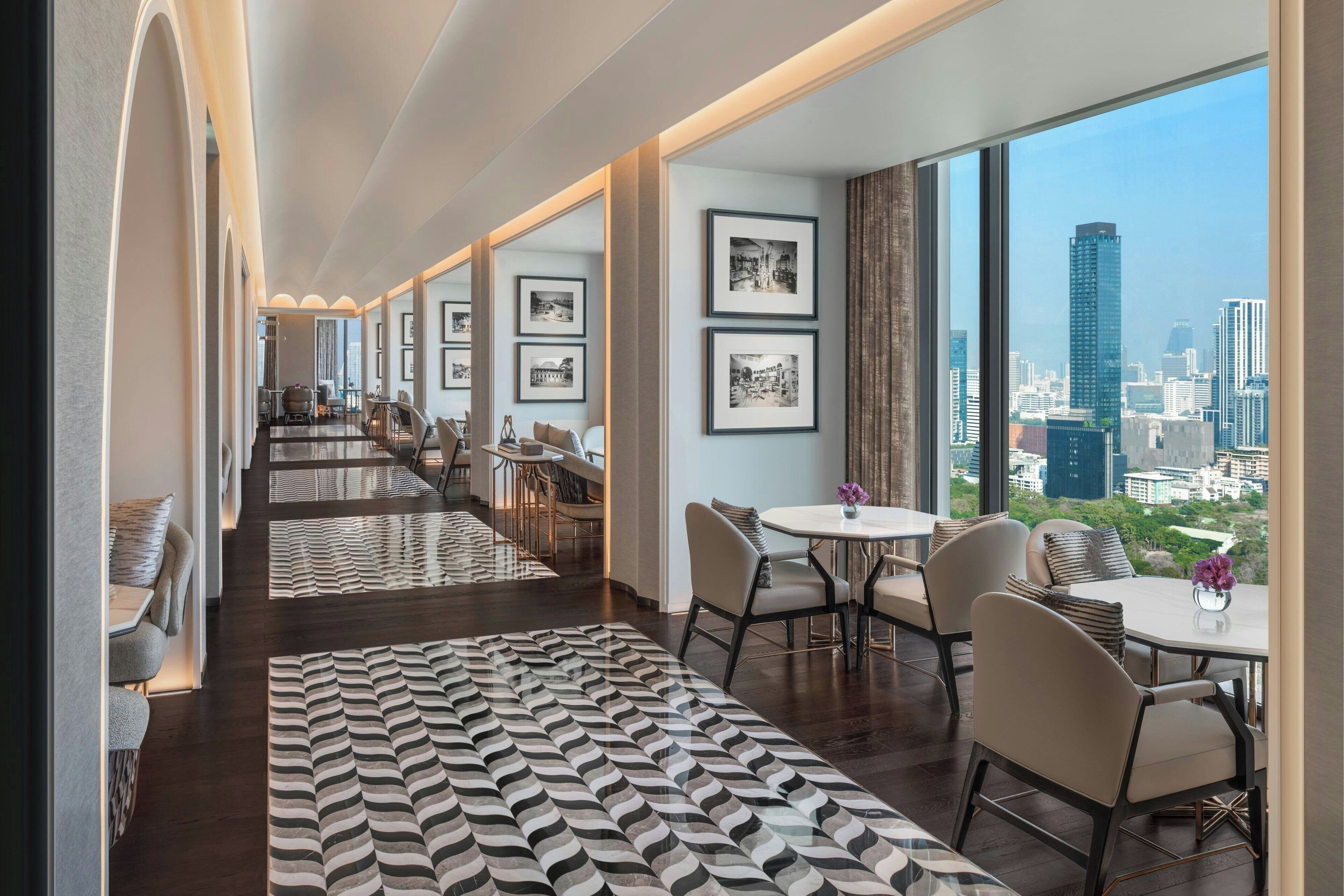 Een moderne hotellobby met een lange gang, een eetgedeelte en grote ramen met uitzicht op de stad.