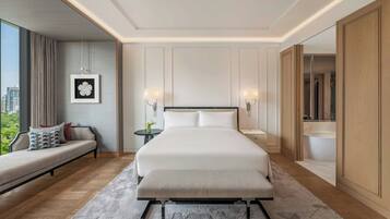 A modern hotel room with a large bed, a sofa, a bedside table, and a view of the city.