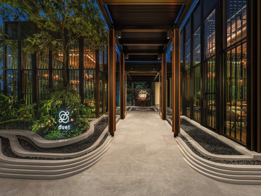 A modern building with a glass facade, a central pathway, and a sign with a logo.