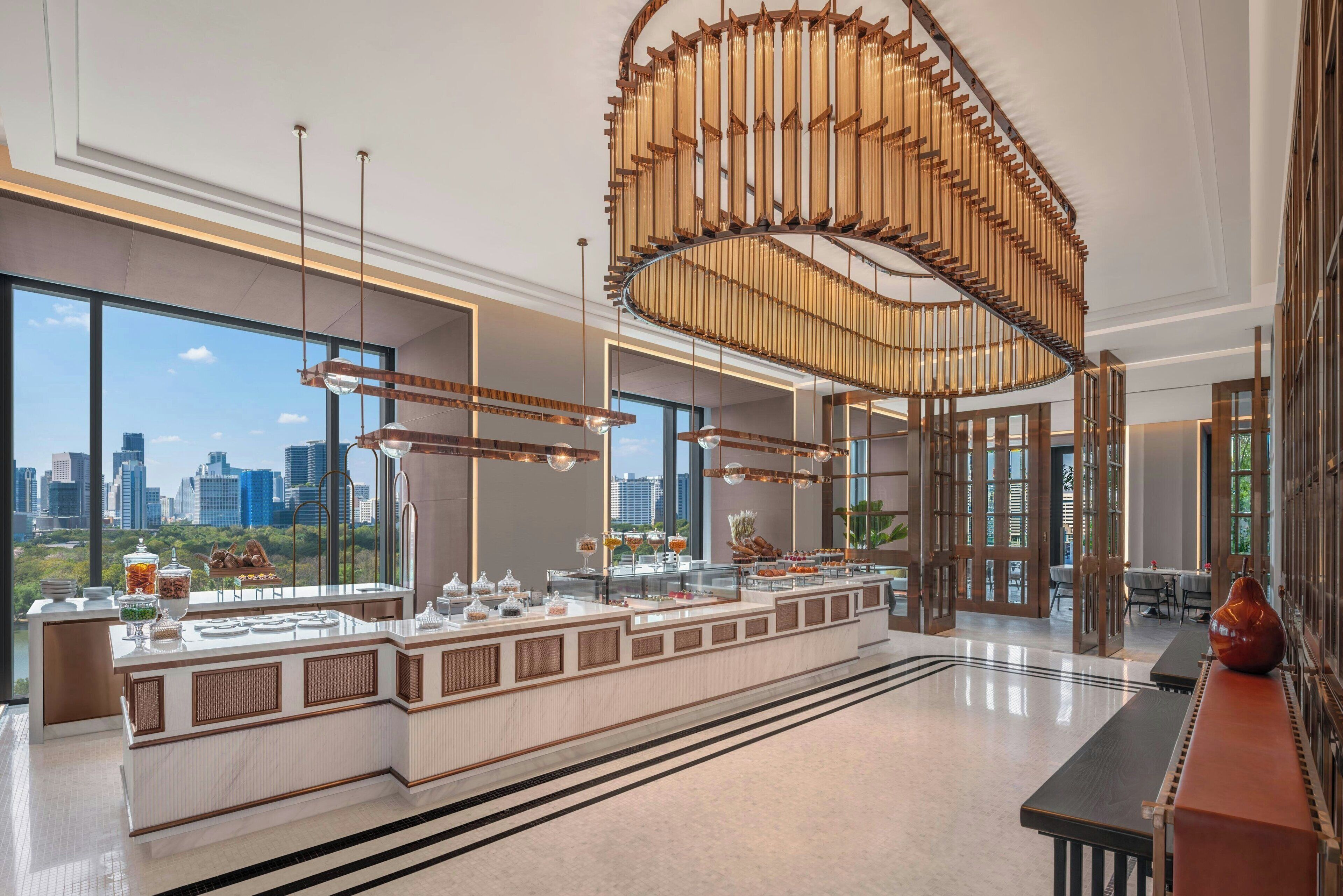 Een moderne hotellobby met een centraal gelegen bar, grote ramen met uitzicht op de stad en moderne verlichtingsarmaturen.