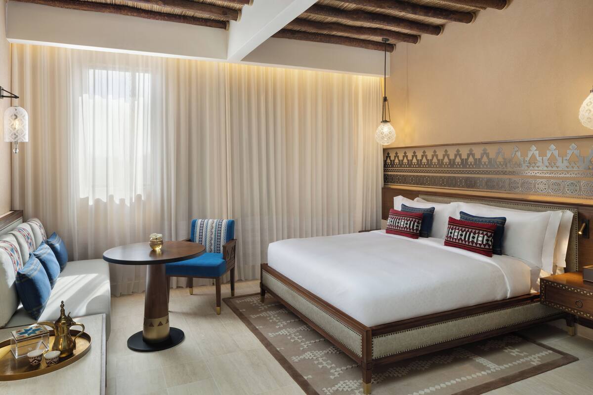 A hotel room with a large bed, a small round table, a sofa with blue cushions, and a decorative wall pattern.
