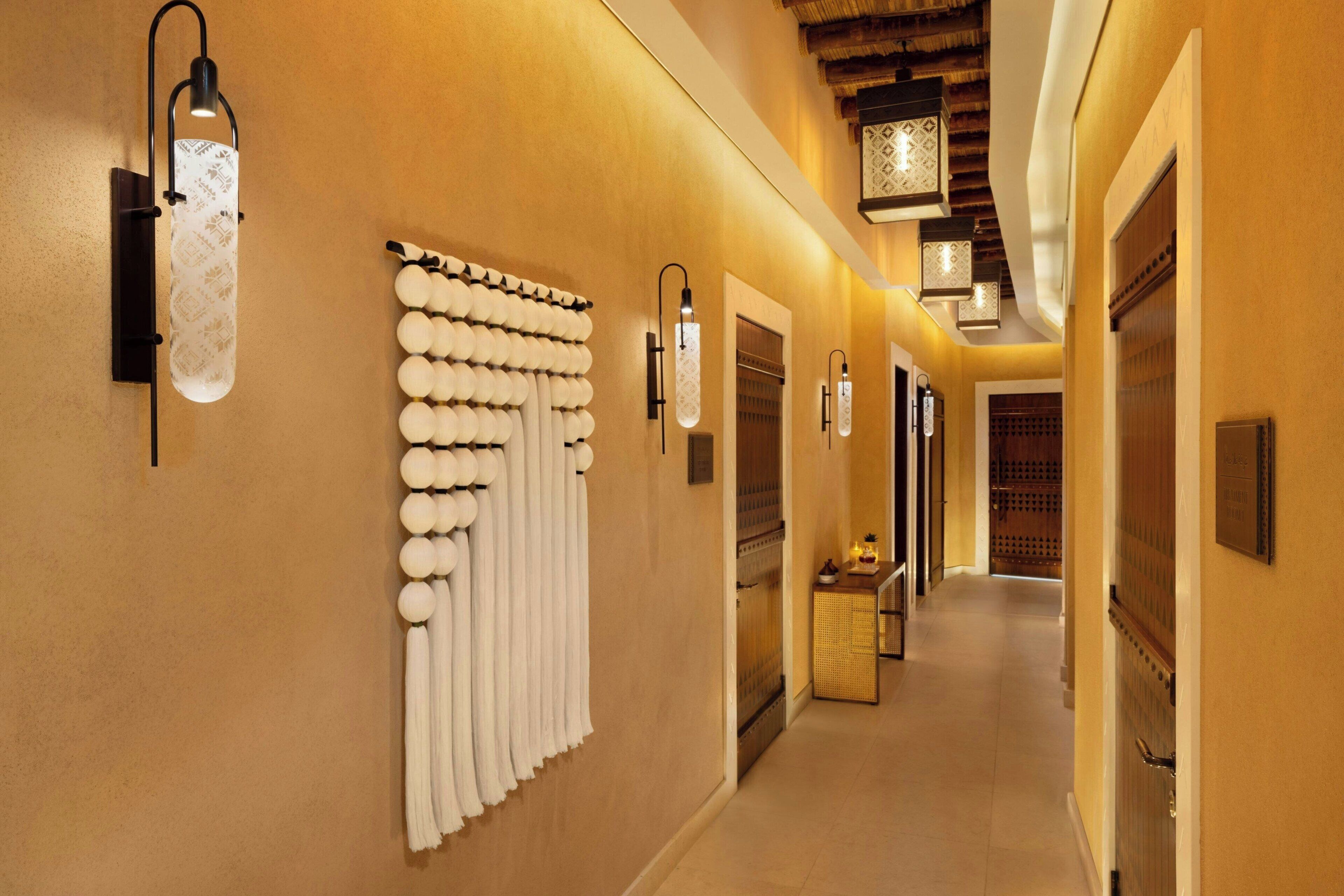 Un couloir d’hôtel aux couleurs chaudes, doté de porte-serviettes fixés au mur et d’un éclairage moderne.