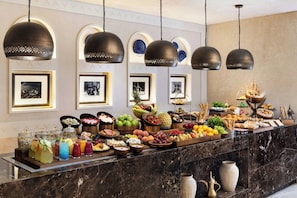 A buffet with various food items and drinks, a marble counter, and hanging pendant lights. - Bab Samhan, A Luxury Collection Hotel, Diriyah (Diryah)