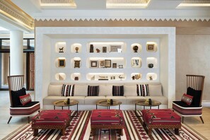 Un salón moderno con un sofá, dos sillones y otomanas, un tapete estampado y una composición de objetos enmarcados en la pared.
