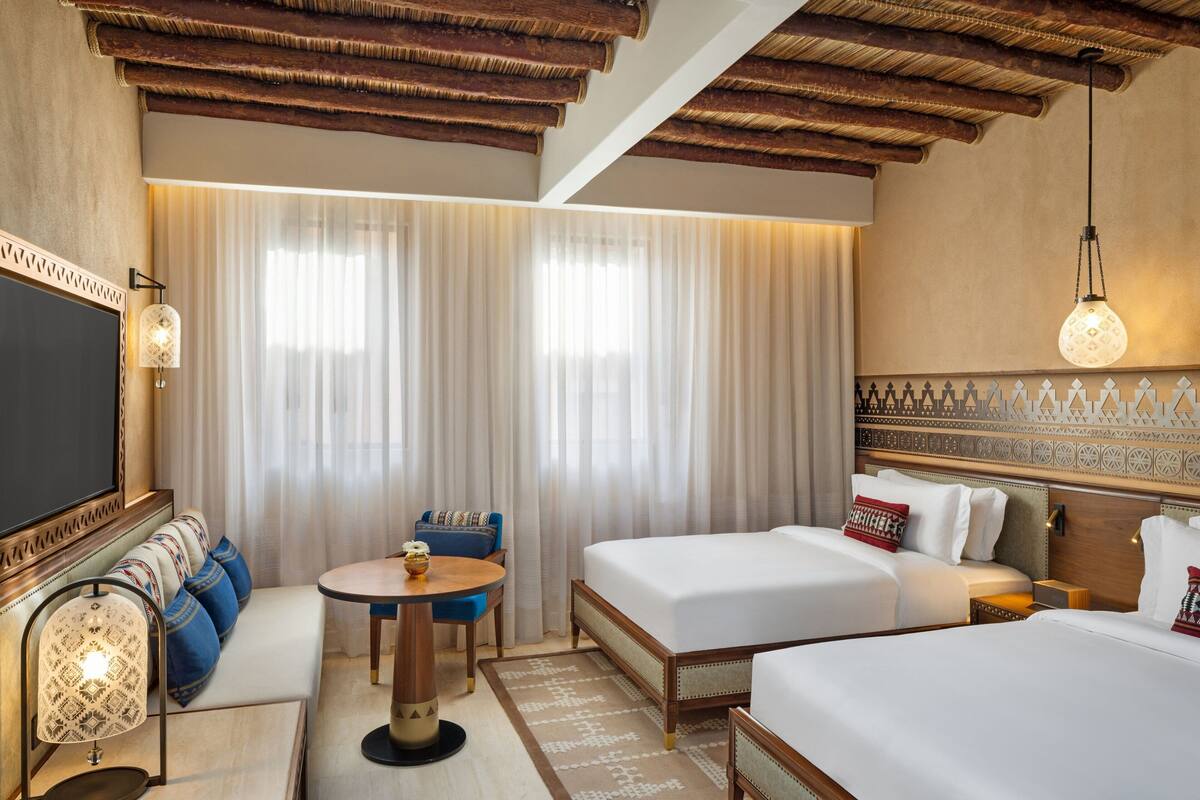 A hotel room with two beds, a sofa, a small table, and a TV.