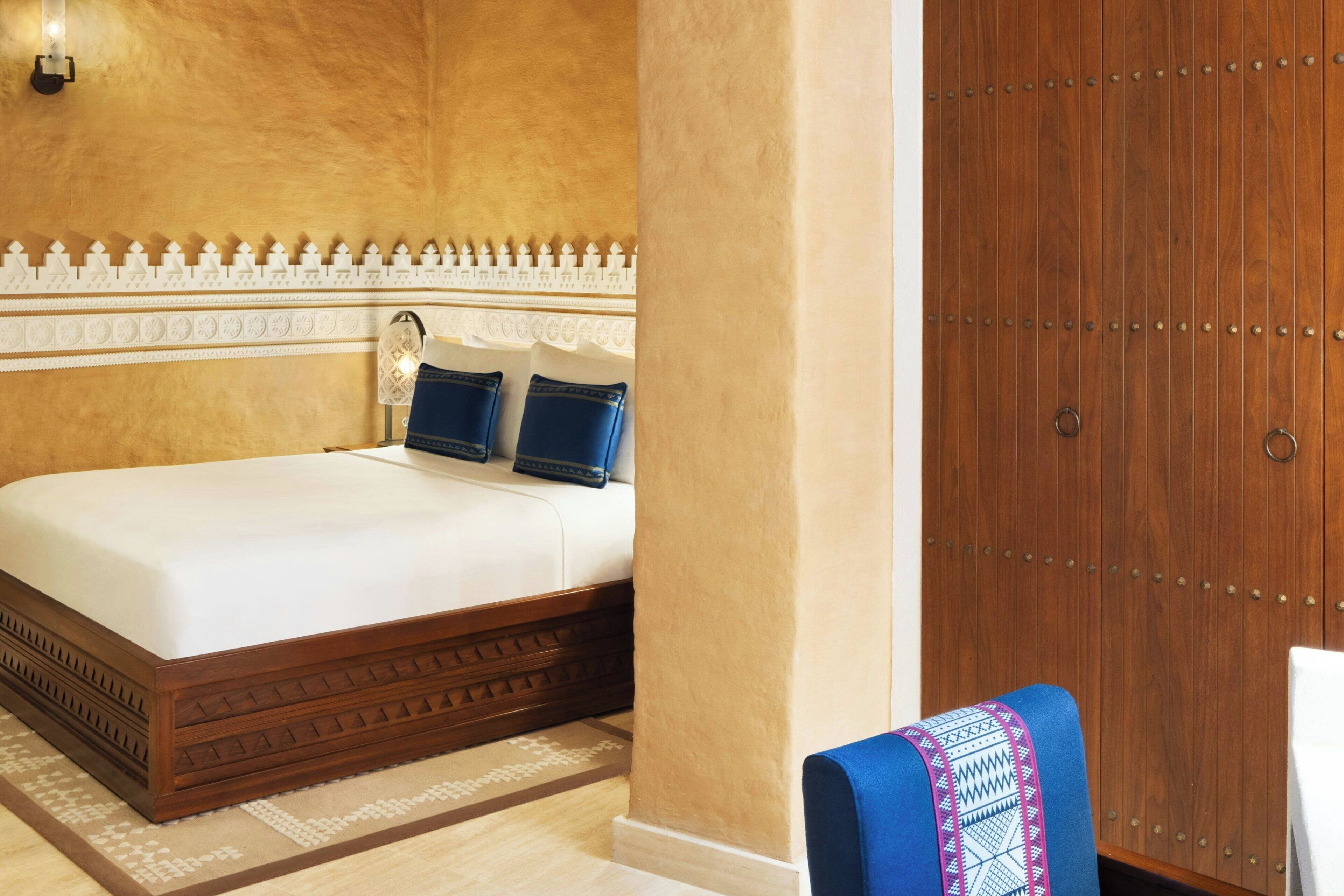 A hotel room with a large bed, a wooden wardrobe, and a patterned rug.