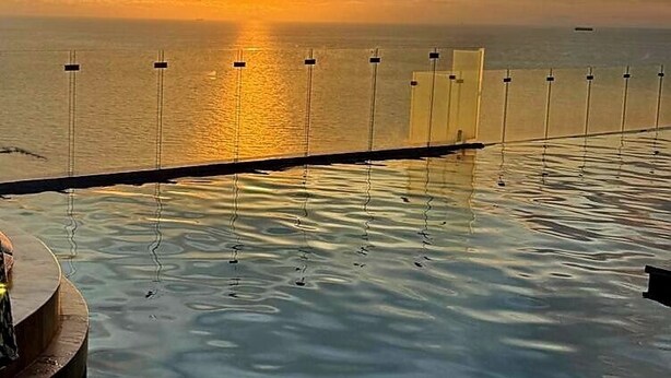 An infinity pool with a view of the sunset over the ocean.
