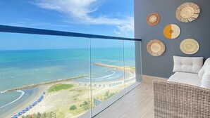 A balcony with a view of the beach and ocean. There are wicker furniture and woven wall decorations.