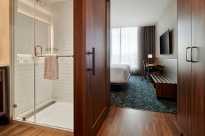 A hotel room with a glass shower, a bed, a desk, and a TV mounted on the wall.