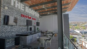 Un bar en la azotea con pared de piedra, televisores de pantalla plana y asientos al aire libre.
