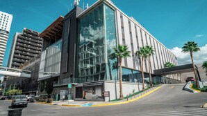 Un hotel moderno con fachada de vidrio, palmeras y un paso peatonal elevado.