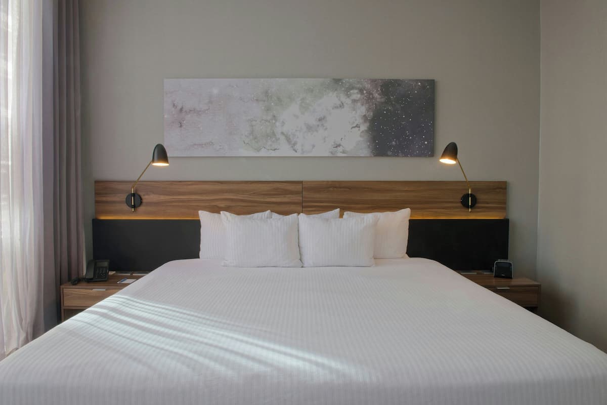 A hotel room with a large bed, two bedside tables, a wooden headboard, and a wall-mounted artwork.