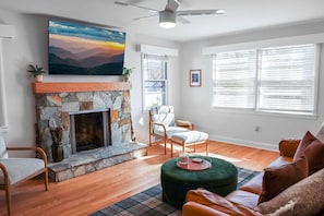 A living room with a stone fireplace, a large painting, and a ceiling fan.