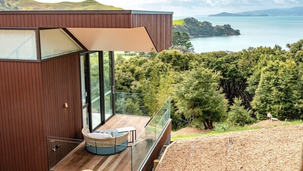 A modern building with a glass balcony overlooking a forest and a body of water.