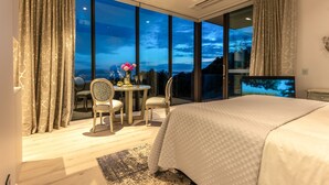 A modern bedroom with a large bed, a small table with chairs, and a TV.