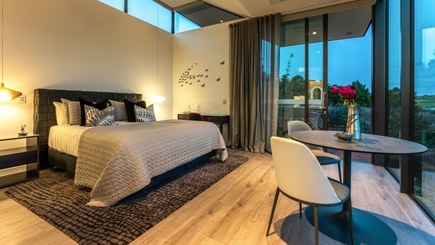 Un dormitorio moderno con una cama grande, mesitas de noche, un escritorio y una zona de comedor con una mesa y sillas.