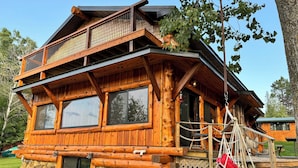 A log cabin with a balcony, large windows, and a hanging chair.