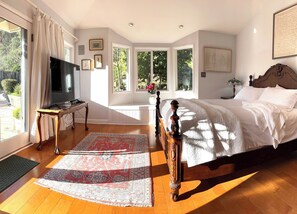 Relax in this serene bedroom with a large bed, television, and a view of lush greenery outside.