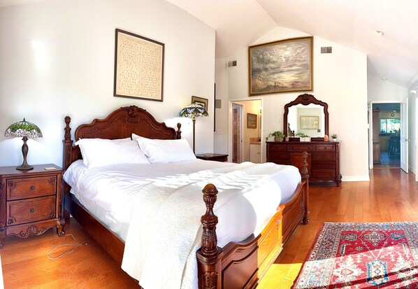 A bedroom with a wooden bed, a nightstand, a dresser, and a large painting on the wall.