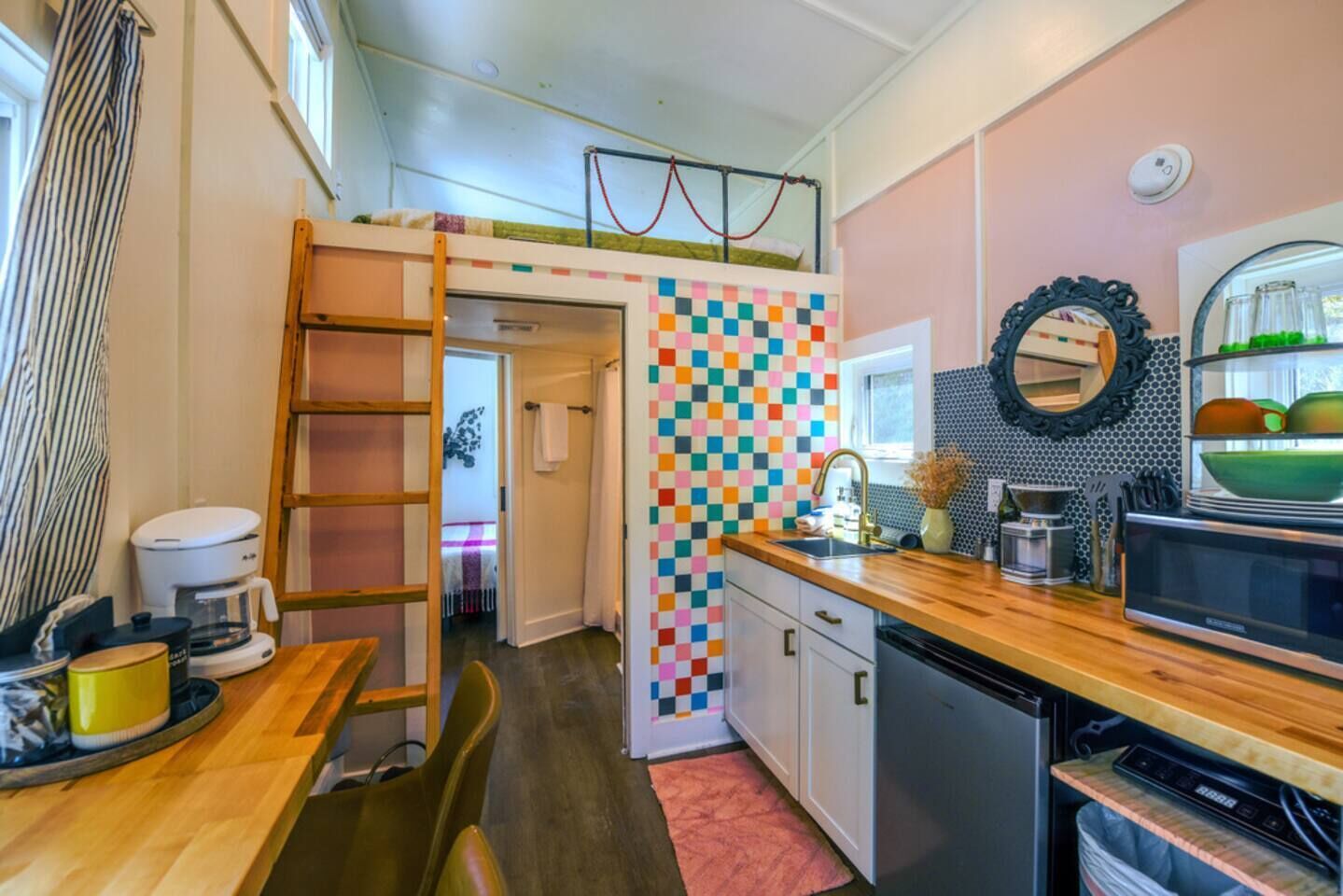 A compact kitchen with a colorful checkered backsplash, a wooden countertop, and a built-in microwave.
